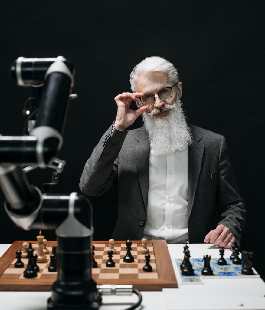 A senior scientist in a suit playing chess with an articulated robot arm on a dark background.